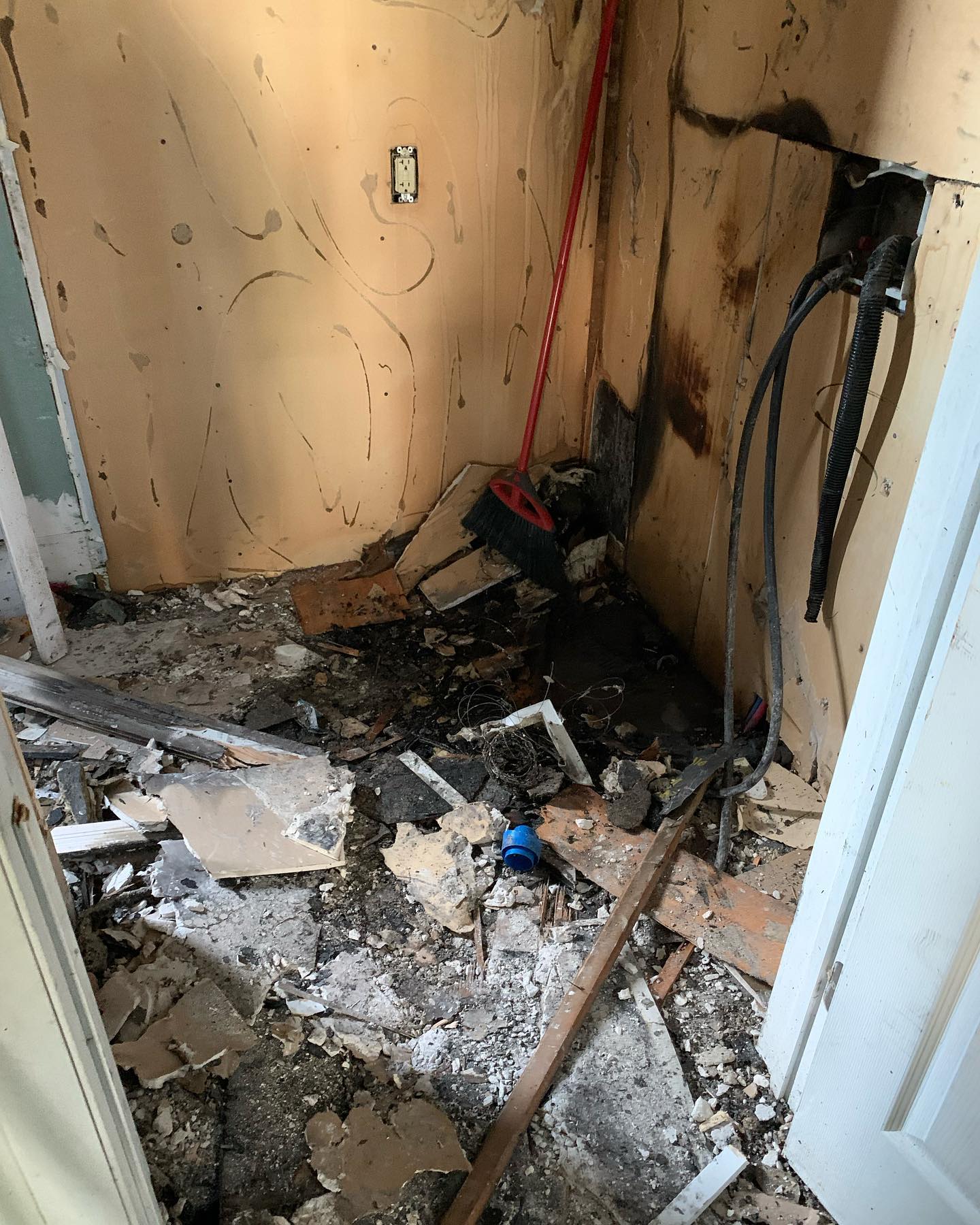 Fire-damaged interior stripped back — scorched wall, exposed wiring, debris across the floor