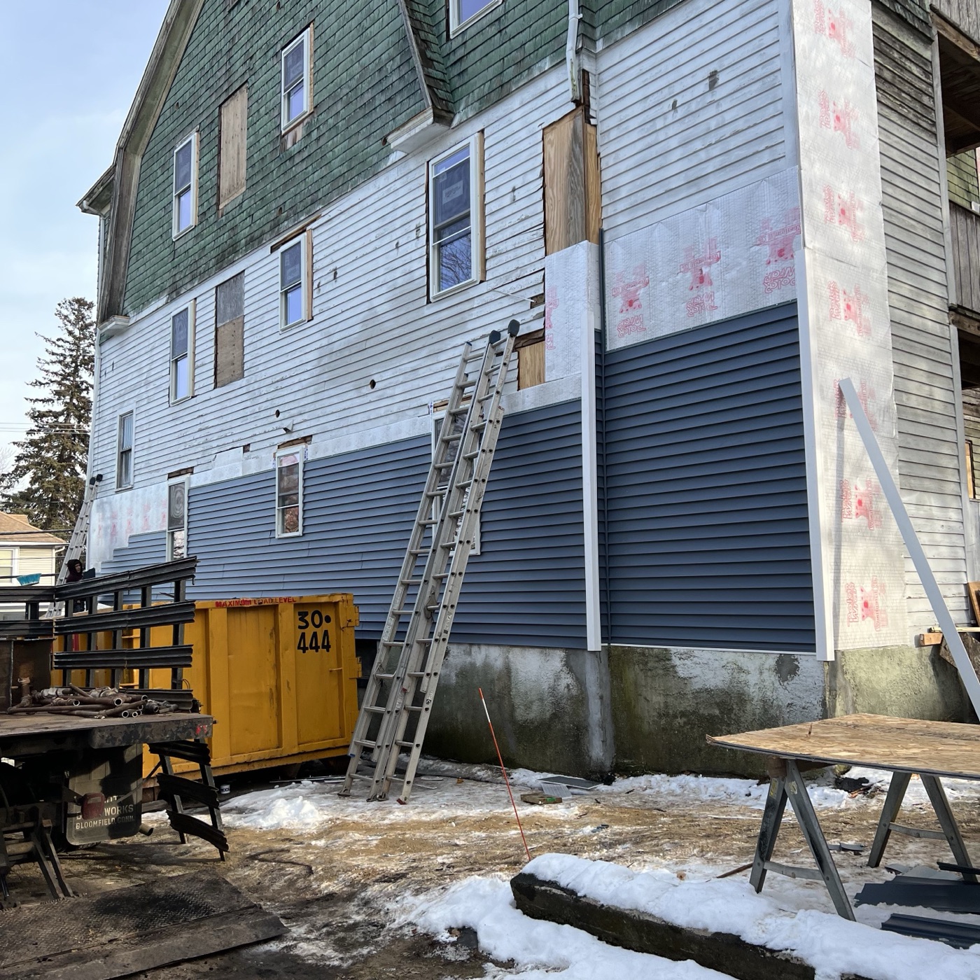 The gable end of 329 Oak Street in January — old clapboard, green shingle and a skip in the yard